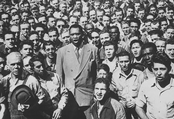 Fig. 5.2. Robeson, a tall and dignified black man wearing a double-breasted suit, with mouth open to sing, is surrounded by a dense crowd of casually dressed men of various skin tones.