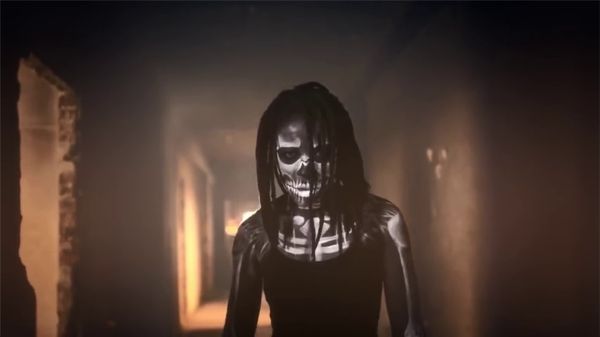 Fig. 8.4. Blakrok is wearing dreadlocks and a tank top and standing in a bare building. An image is projected onto her body, making her look like a skeleton.