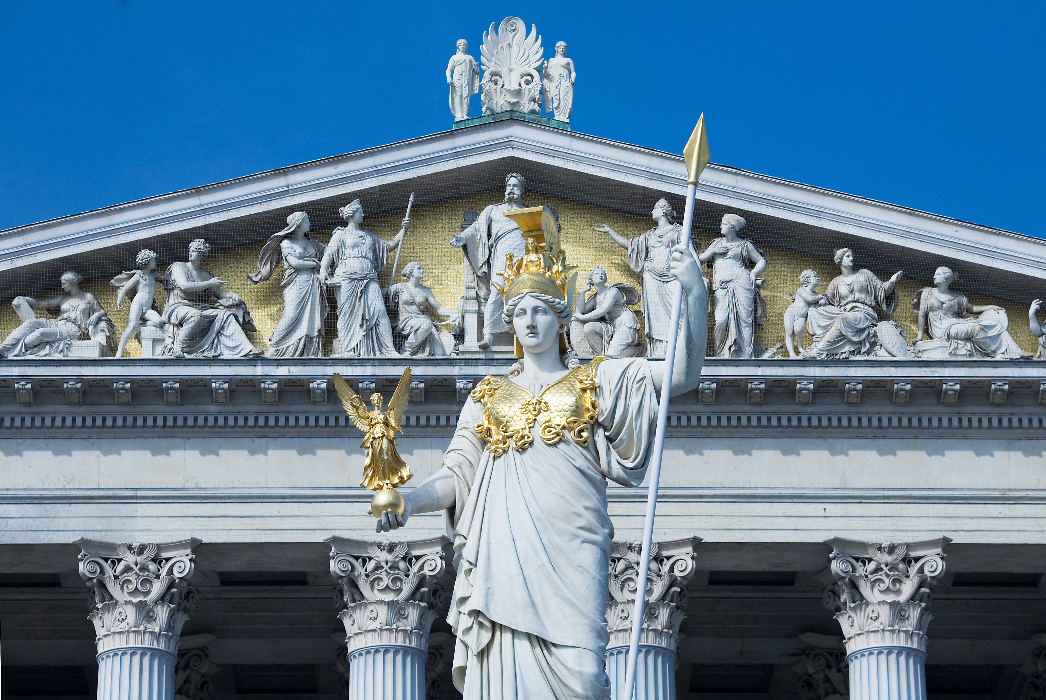 Statue of Athena in front of a Greek style building, with columns and statues in the pediment.