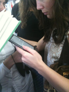 Woman standing, reading on a Kindle on a crowded public transit train