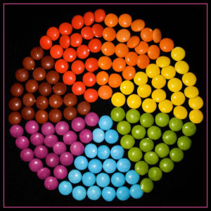 round candies in bright colors arranged in triangle wedges to form a color wheel, on a black background