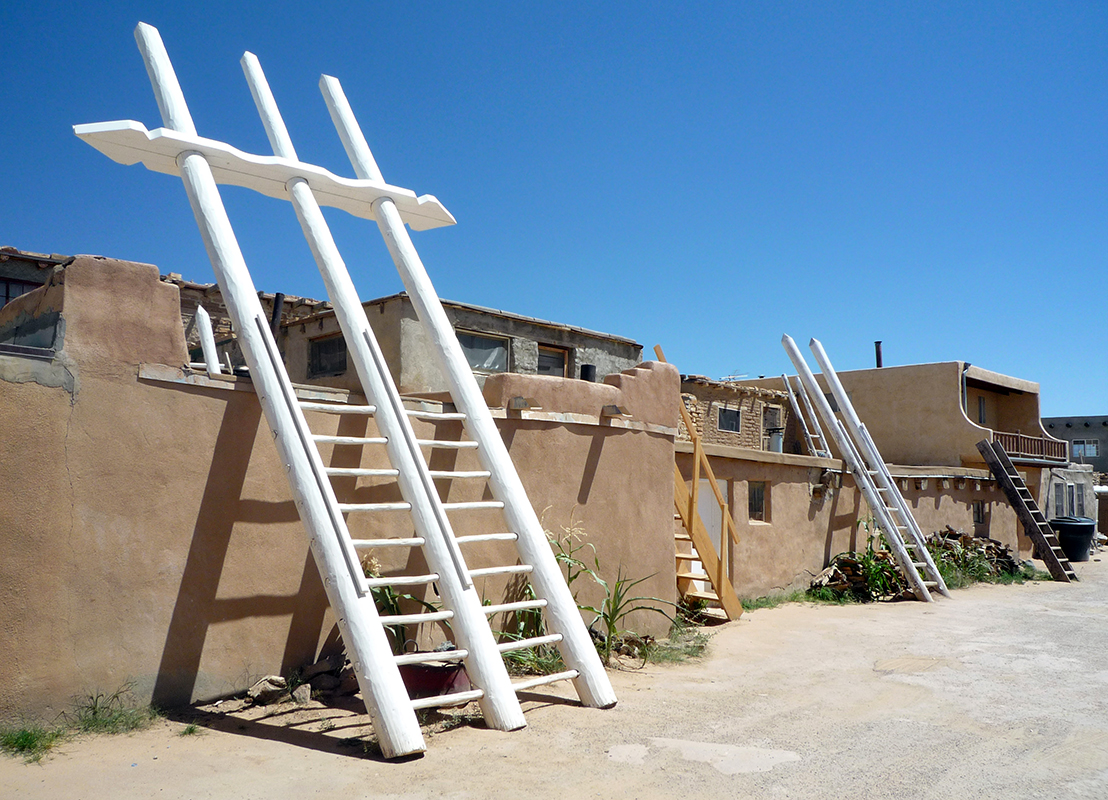 Acoma Pueblo street with adobe buildings and ladders that lead to the upper story entrances to kivas (sacred ceremonial spaces)
