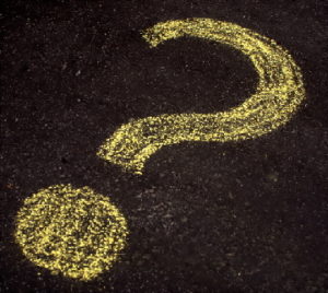 Question mark drawn in yellow chalk on black pavement
