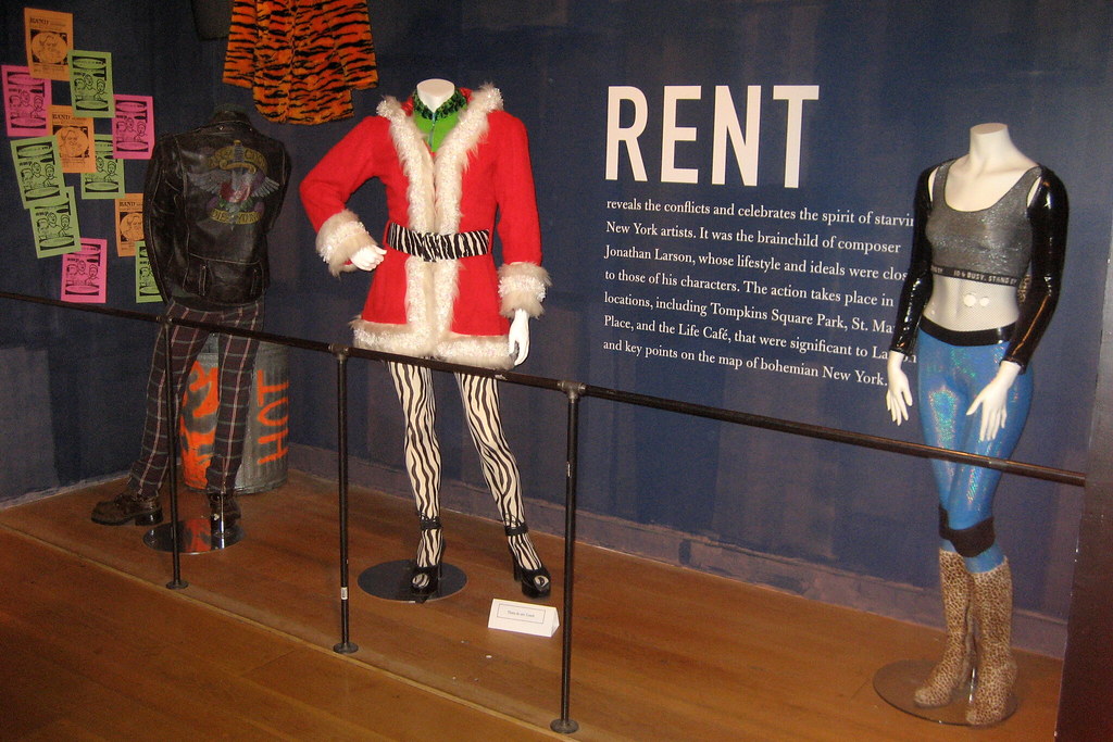 Three mannequins wear costumes from the musical "Rent" in a display.