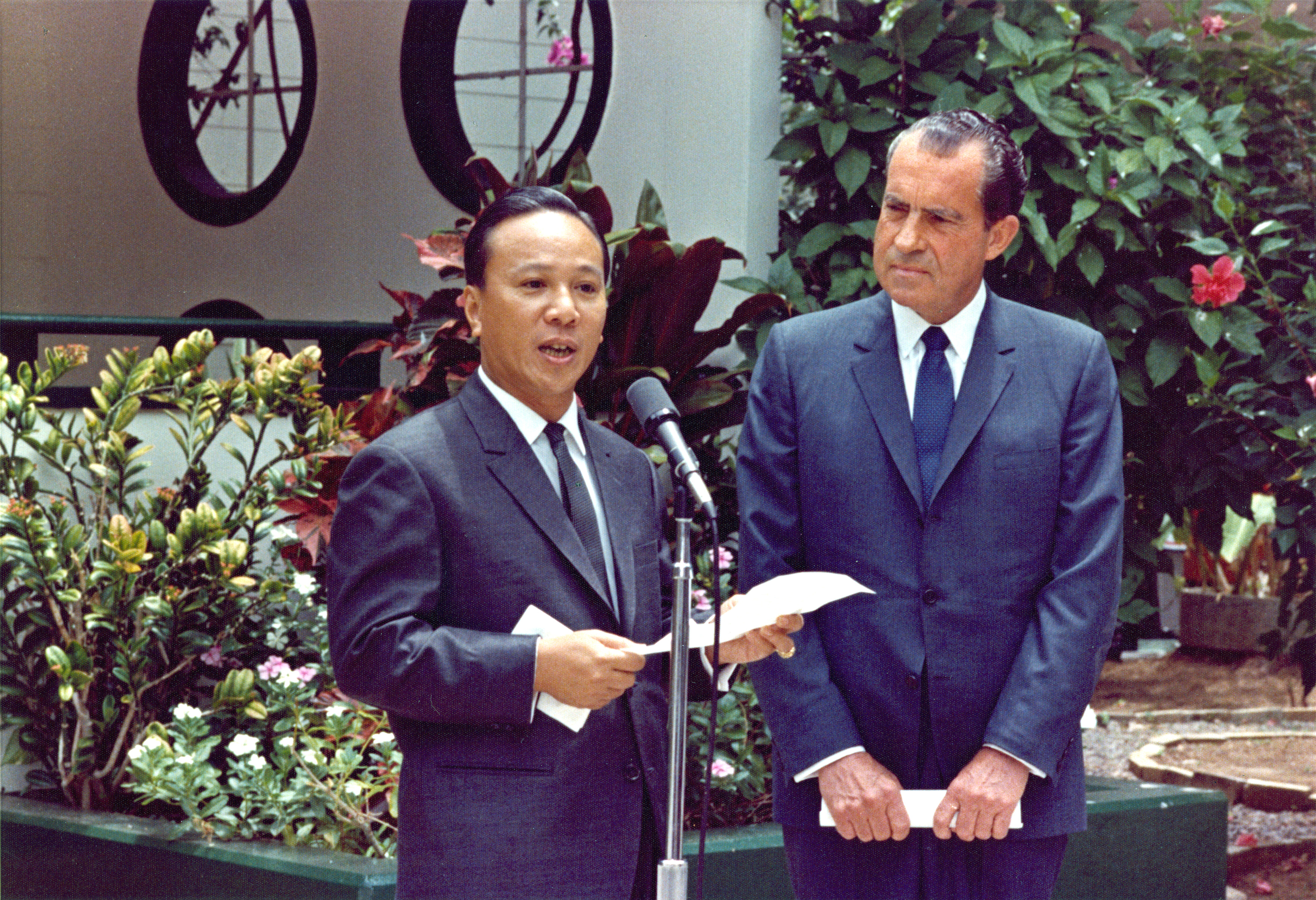 President Nixon and South Vietnamese dictator Nguyễn Văn Thiệu are dressed in suits and standing in front of a microphone stand to make a joint statement at Midway Island. Details in text.