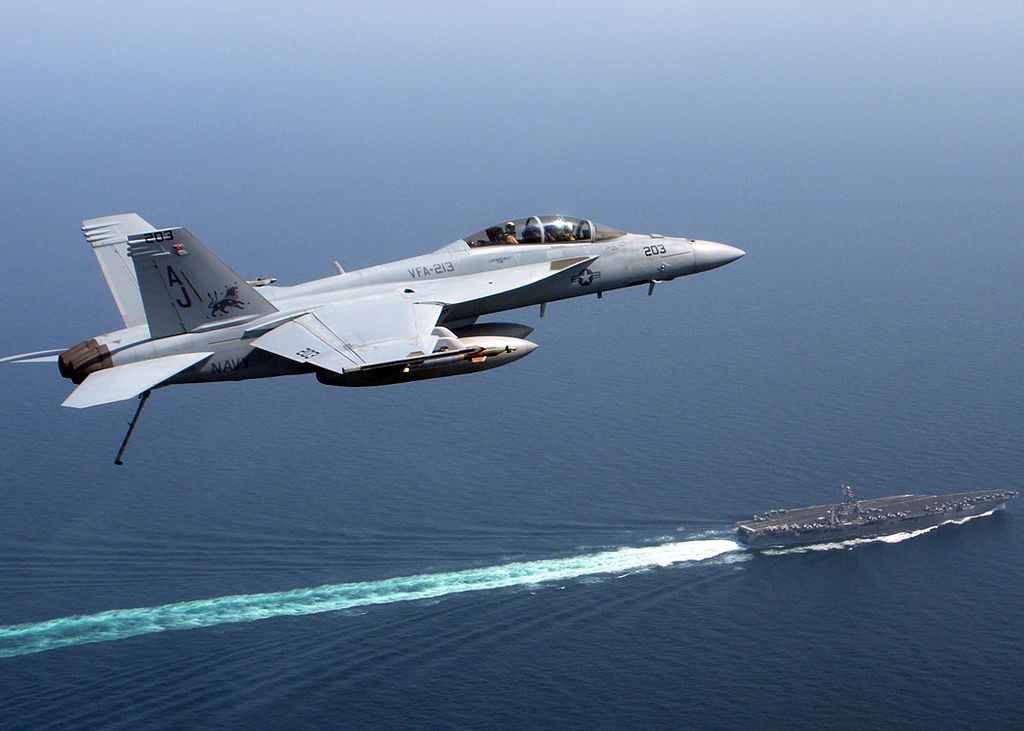 "An F/A 18 Super Hornet, assigned to the "Blacklions" of Strike Fighter Squadron (VFA) 213, flies over the aircraft carrier USS Theodore Roosevelt (CVN 71) during flight operations." by Lt. Cmdr. Johnnie Caldwell, U.S. Navy is in the Public Domain