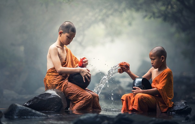 Two young Buddhist monks in orange robes performing a water ritual.