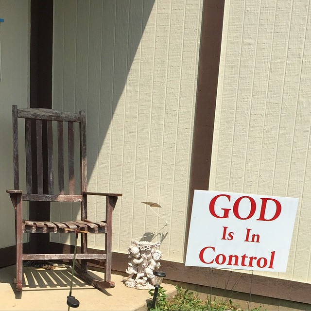 Image of a wooden rocking chair beside a sign that reads "God is in Control"