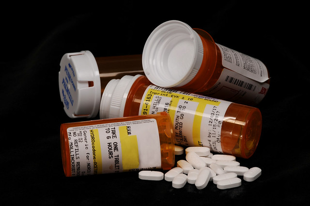 Image of several prescription drug bottles with white pills spilling out