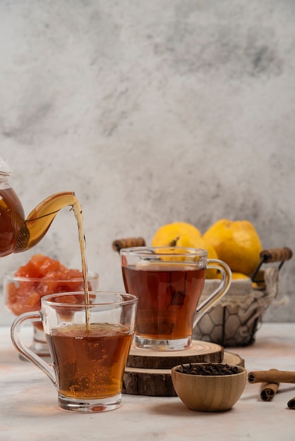 Free photo transparent glass teapot pours tea in glass mug on marble table.