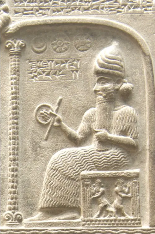 A picture of a white stone carving is shown. Designs are carved along the top and wavy lines along the bottom. On the left there is a tall, thin, column carved with squares and three curly posts on top. Inside the designs, a carving of a man is shown in long robes etched with wavy lines, a long wavy beard, a tall pointy, striped hat, and holding a ring and stick in his right hand. He sits on a box decorated with etchings on the perimeter. Inside the box is a carving of two people with beards facing away from each other. Above the ring and stick in the man’s hand there are two rows of etchings in a rectangle and three circles above that, the first showing a moon, the second and third showing a sun. The background is smooth stone.