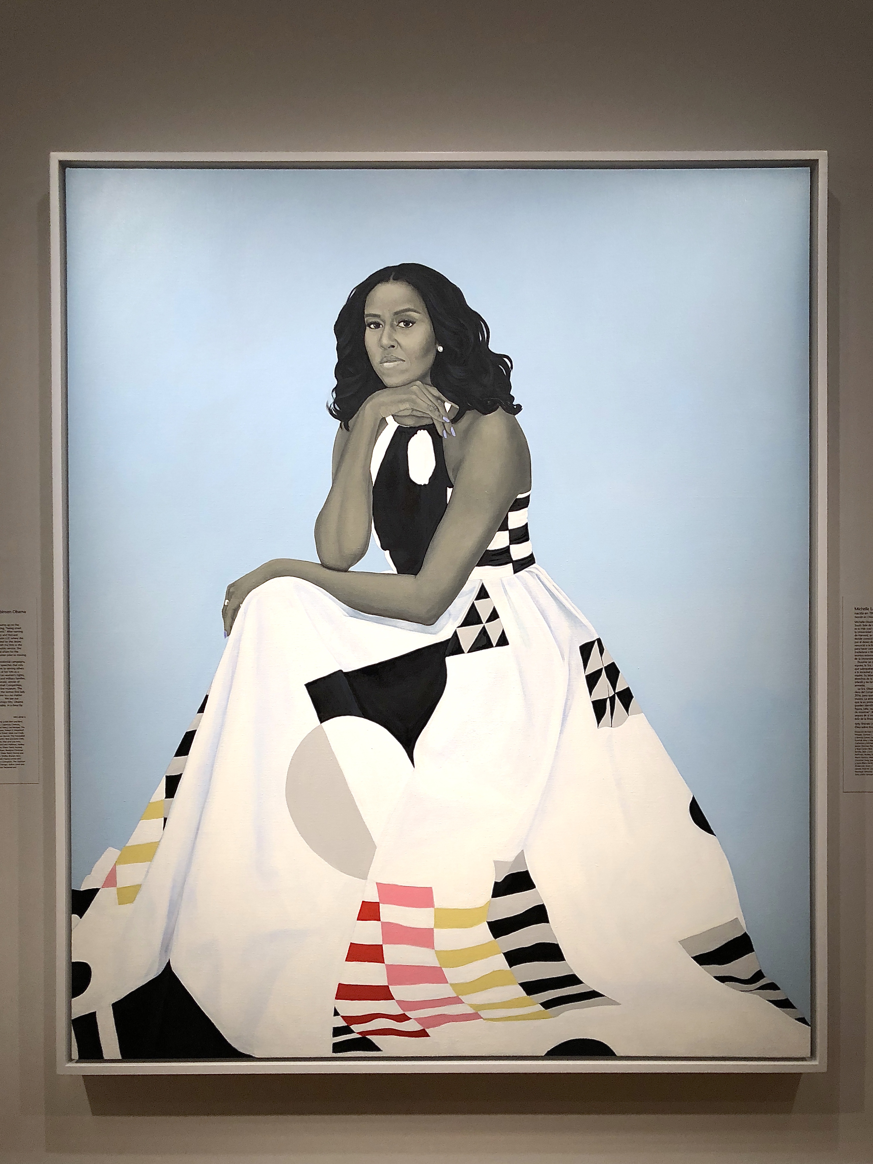 A woman sitting in a white dress with some shapes of color on the dress