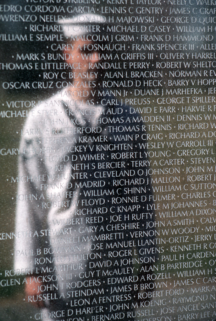 a man dressed like a sailor looking at a black wall with names engraved