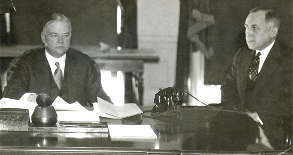 Uma fotografia mostra Herbert Hoover sentado à esquerda em uma mesa com o assessor Theodore Joselin. A mesa contém papéis e um telefone. A expressão facial de Hoover é sombria e distraída.