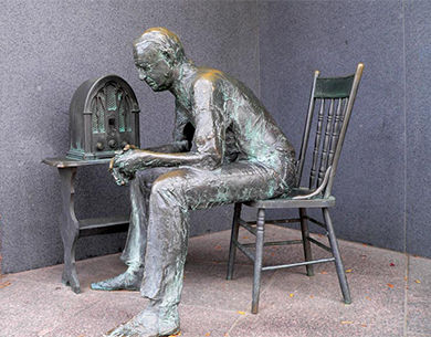 雕塑描绘了一个男人坐在收音机旁边的椅子上。