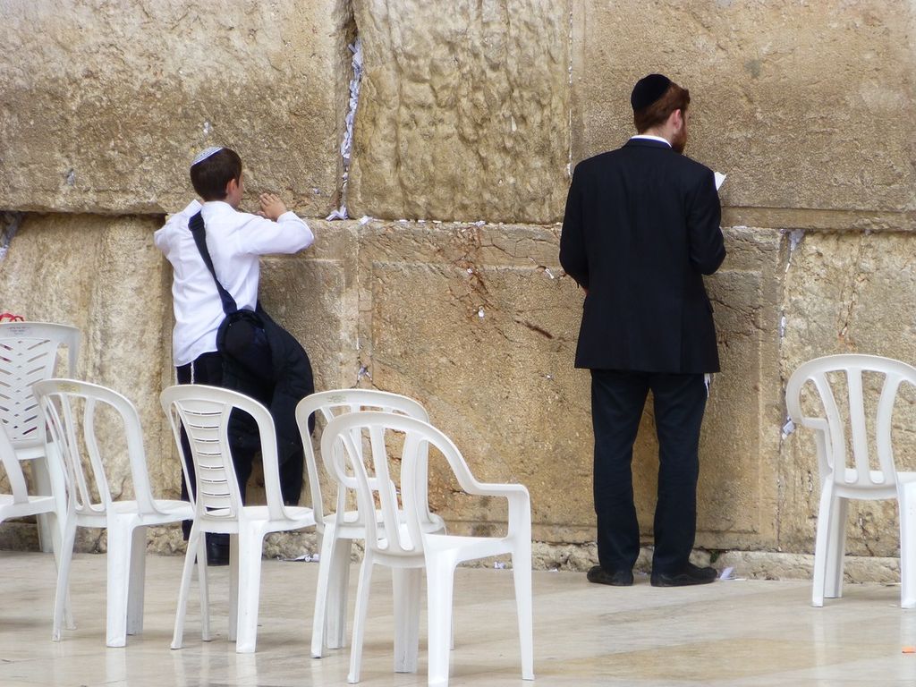 Young Jewish boy and man each wearing a yarmulke pray at the Wailing Wall in Jerusalem.