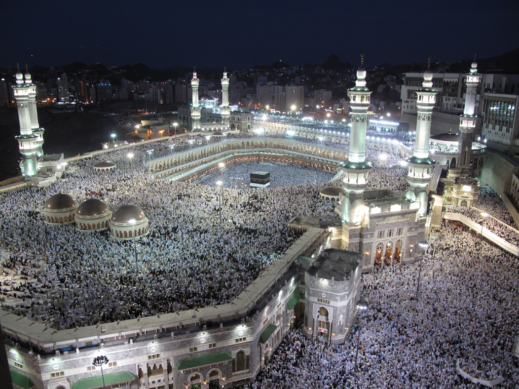 Thousands of Muslim congregants dressed in white converge at the Grand Mosque in Mecca. Moving in a circular pattern, worshippers make their way to the interior of the Mosque where the rectangular Ka’aba sits.