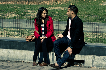 Une femme et un homme s'assoient sur un banc au parc. L'homme parle à la femme qui a un visage inquiète ou peut-être ennuyé.