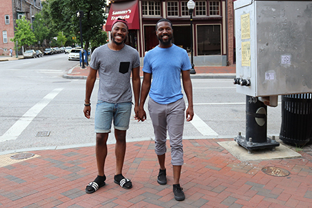 Deux hommes Afro-Américain se tiennent par la main et sourient. Ils se trouvent sur le trottoir au centre-ville.