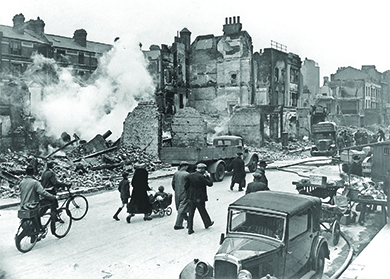 Una fotografía muestra una calle londinense destruida en la que la mayoría de los edificios se han reducido a escombros; los ciudadanos pasean con bicicletas y un niño en un carrito