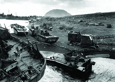 تظهر صورة القوات الأمريكية وهي تصل إلى الشاطئ على الرمال المظلمة لإيو جيما. يظهر جبل سوريباتشي في الخلفية.