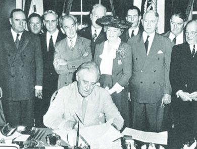一张照片显示富兰克林·罗斯福坐在办公桌前签署地理标志法案，被国会议员包围。