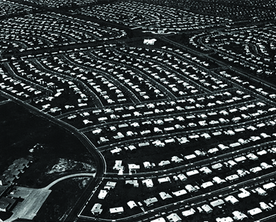 Une photographie aérienne de Levittown, en Pennsylvanie, montre des hectares de terrain avec des maisons standardisées disposées en rangées soignées.