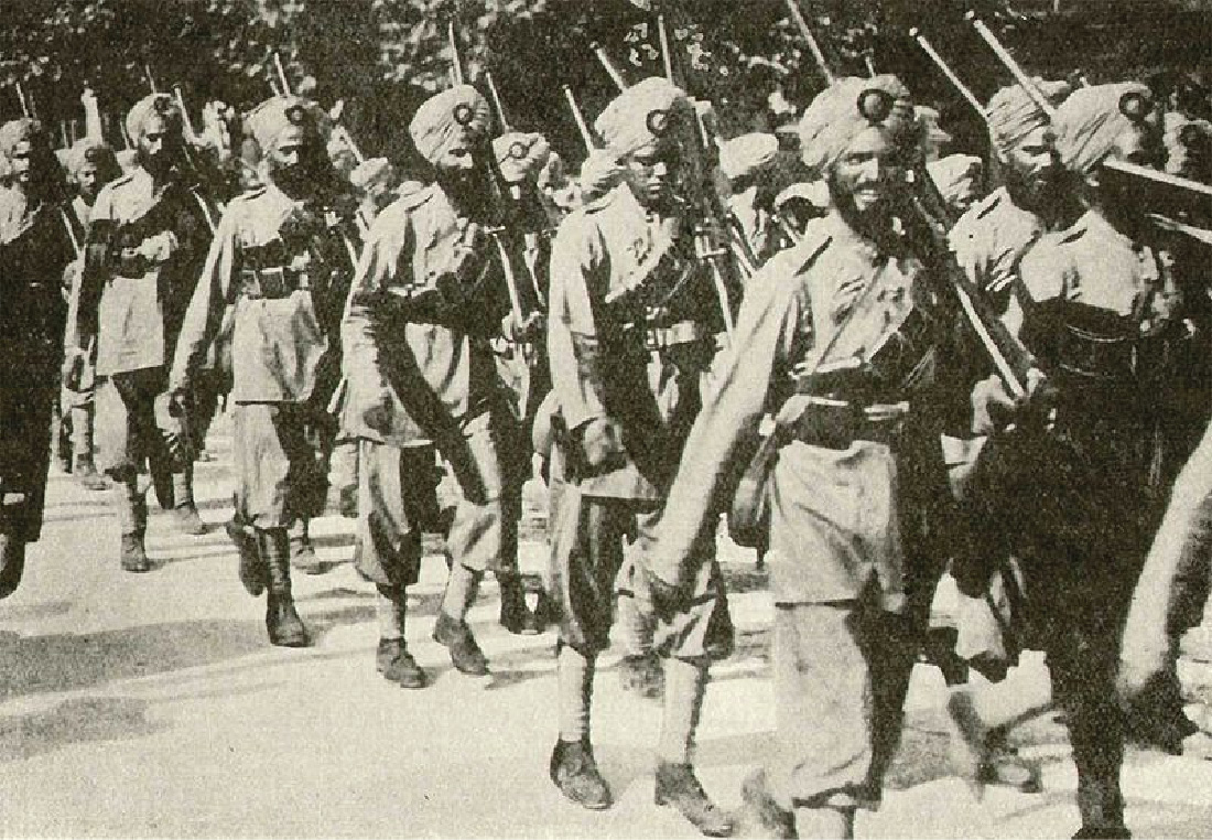 Troops march in a line. They carry rifles and wear military uniforms. They all wear turbans, and most soldiers have beards.