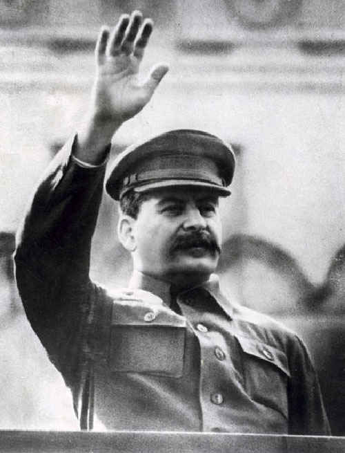 A man wears a military style uniform and waves with his right hand.