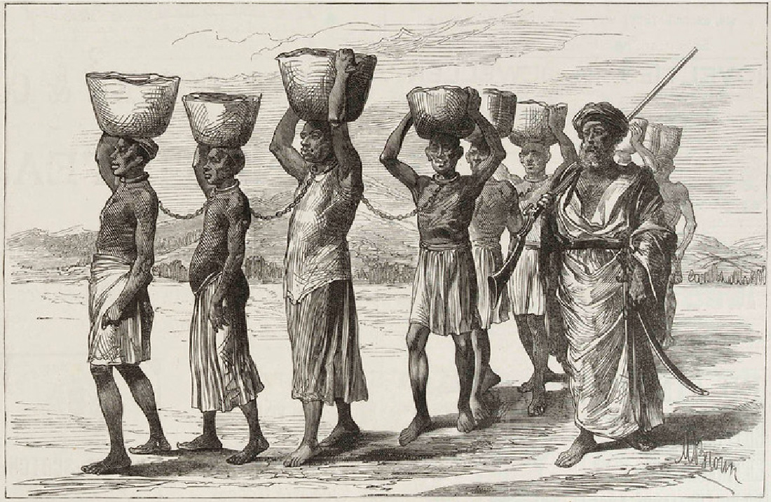 A drawing shows ten people walking. Nine of the people walk in a line and are chained together by their necks. They carry baskets on their heads and are dressed in single pieces of cloth. A man with a beard walks next to them. He carries a gun and a sword and is fully clothed and wears a turban on his head. The ground is hard and dry and there are hills in the background.