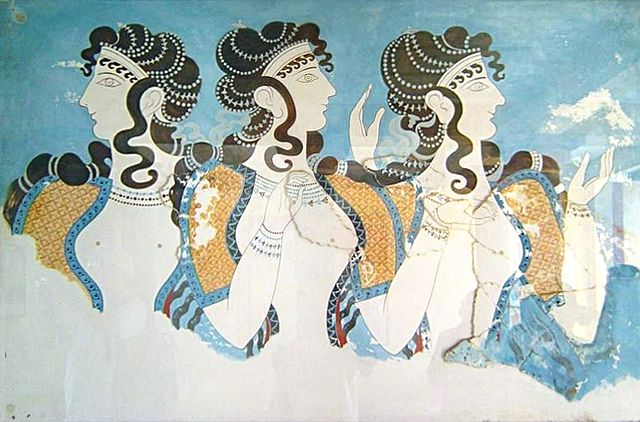 This is a color photograph of a fresco from the complex at Knossos. It depicts a popular fashion for Minoan women—short-sleeve dresses with flounced skirts whose bodices were open to the navel, allowing their breasts to be exposed. The women's faces are in profile view and their bodies are in frontal view.