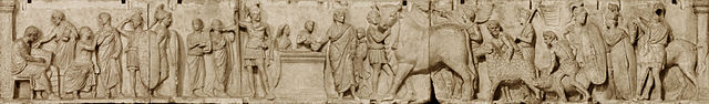 This is a photo of a panel from the Altar of Domitius Ahenobarb, a marble bas-relief that depicts the different stages in a census of the Roman citizen body. In the first scene, the oath-taker sits holding a tablet to record the name and property of a line of men before him. The second scene shows the religious ceremony that legitimized the census. A censor presides, placing his hand on a statue of Mars, depicted in full armor. A bull, a ram, and a pig are led to the censor for sacrifice. The final scene depicts two soldiers with shields and a horse.