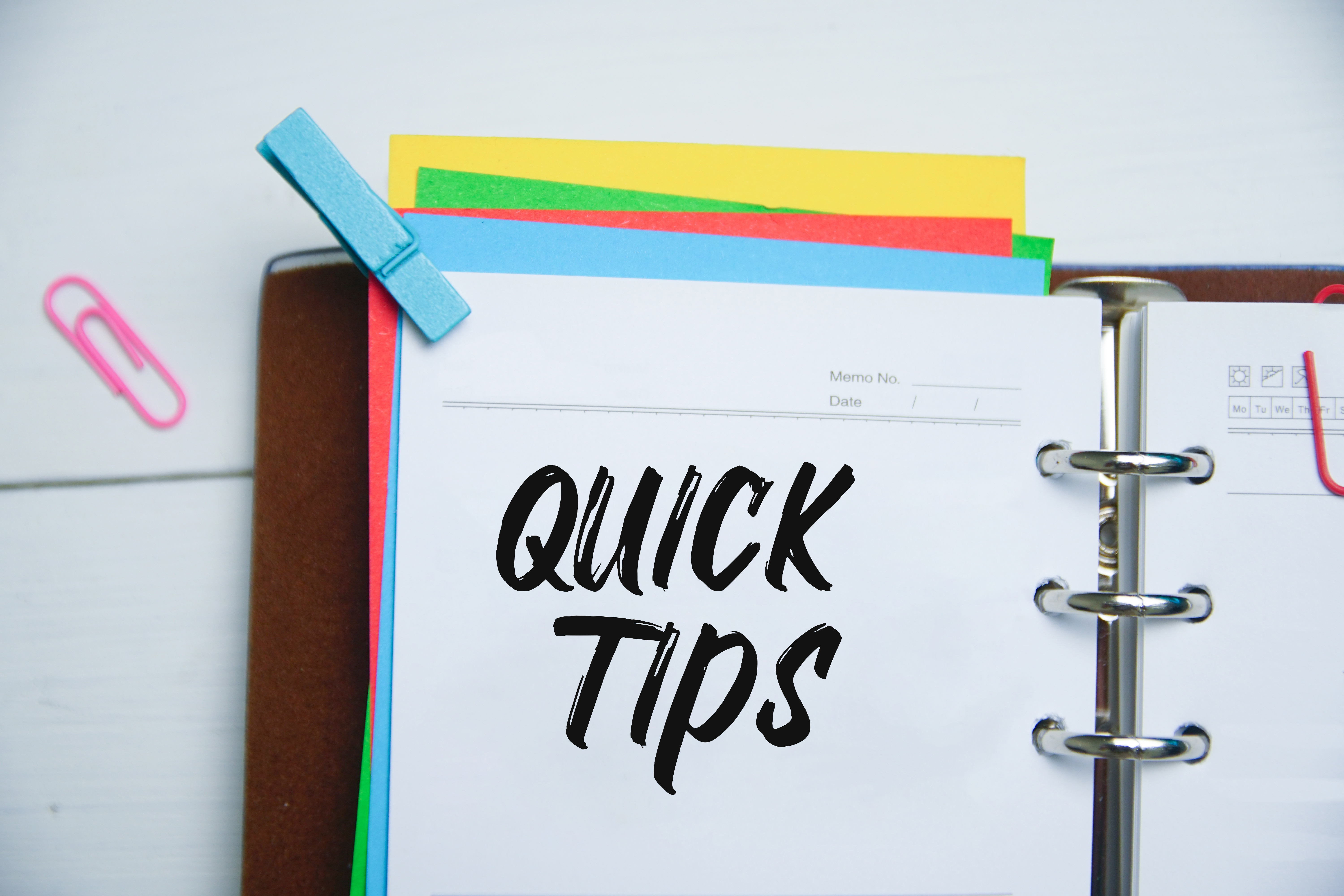 Open notebook with colorful pages, a blue clip, and paper clips. Quick Tips is written in bold on one page.