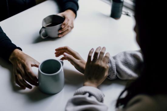 Comfy setting showing two people's hands reaching out to each other over a table, with coffee