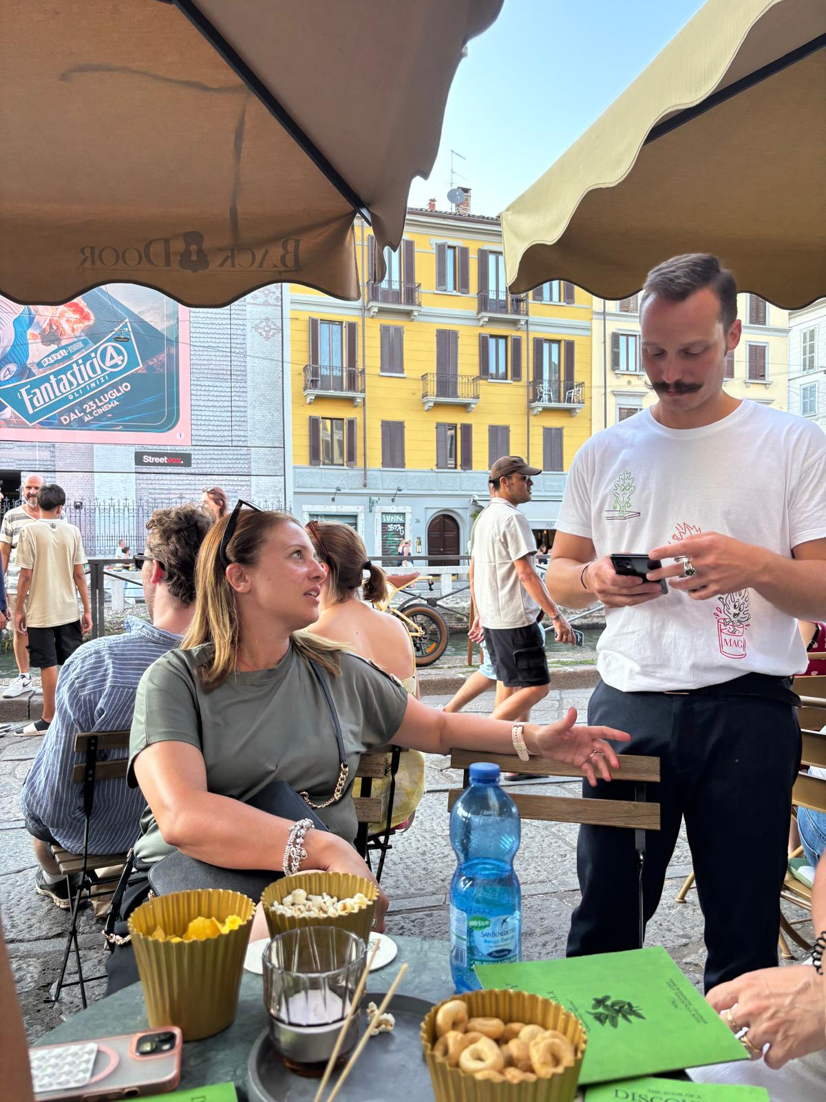A waiter taking an order from a customer at an outdoor bar on the Navigli canals in Milan.