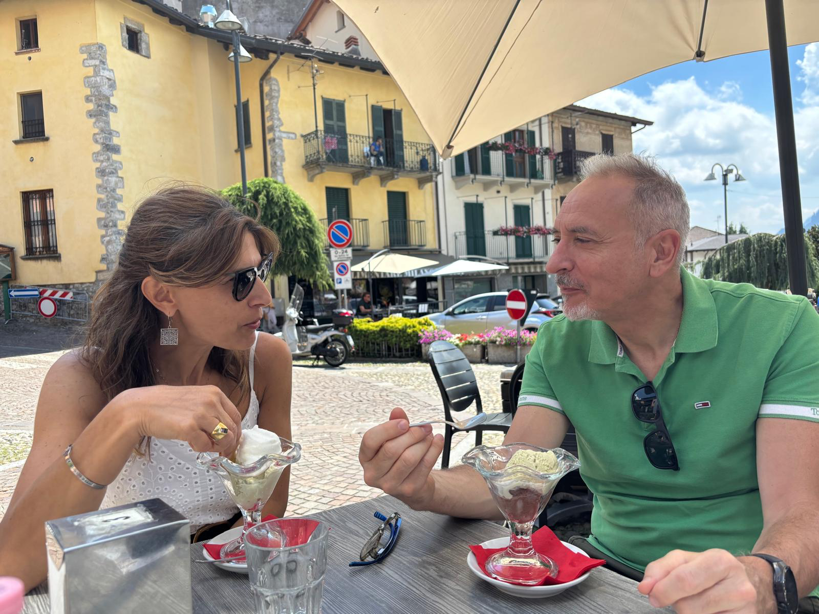 Two people sitting at an outdoor bar in a mountain village, eating ice cream.