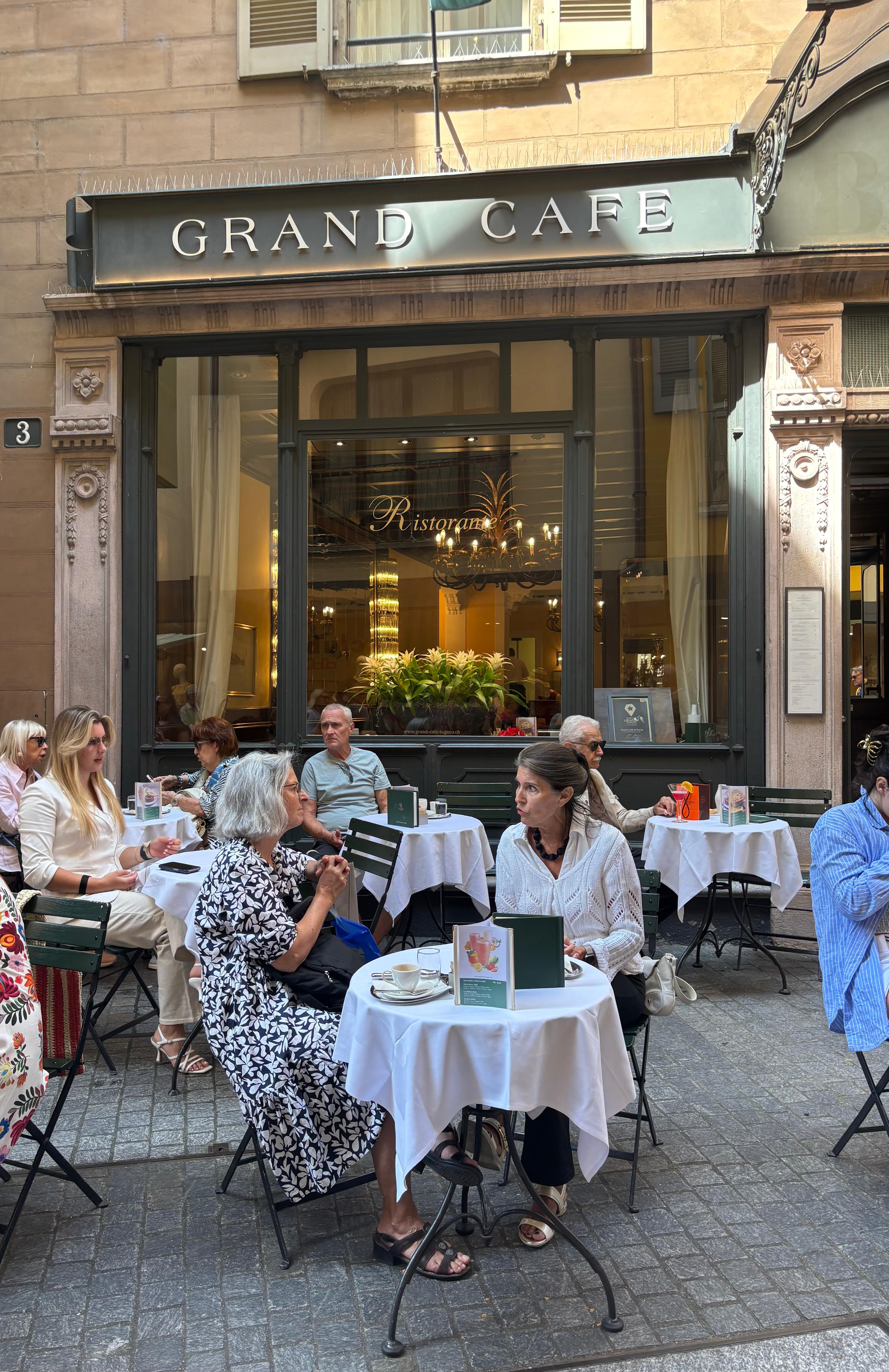 People sitting at an outdoor historical caf&eacute;, chatting and enjoying breakfast in a relaxed atmosphere.