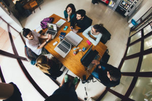 Photo looking down on a group of students around a table, with several open laptops in front of them