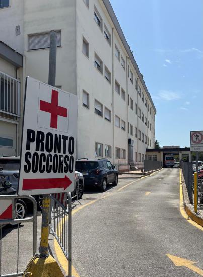 A hospital entrance with a red cross and a sign that says ‘Pronto Soccorso’ (Emergency Room)