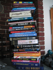 Photo of a stack of roughly 20 textbooks. Prominent titles include Gray's Anatomy, Pathology, Fundamental Neuroscience, and Calculus.