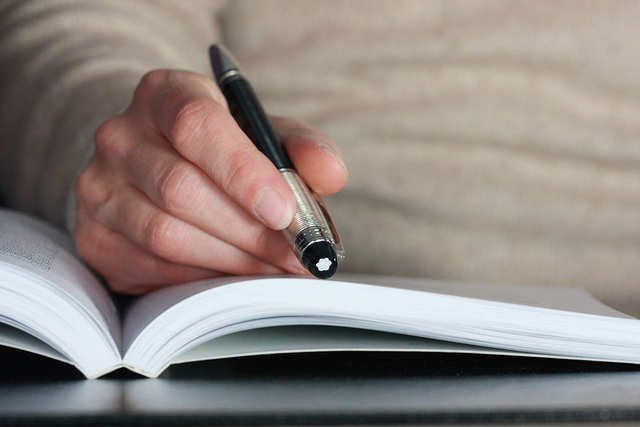 Photo of a hand holding a pen over an open book