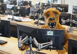 Photo of a person in a lion mascot uniform sitting in a computer lab