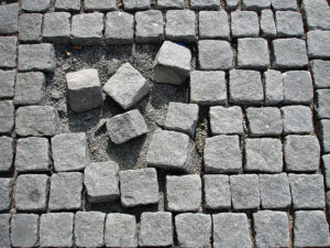 Photo of stone path pavers. Most of them are laid out orderly, but a central cluster are in disarray, with several missing.