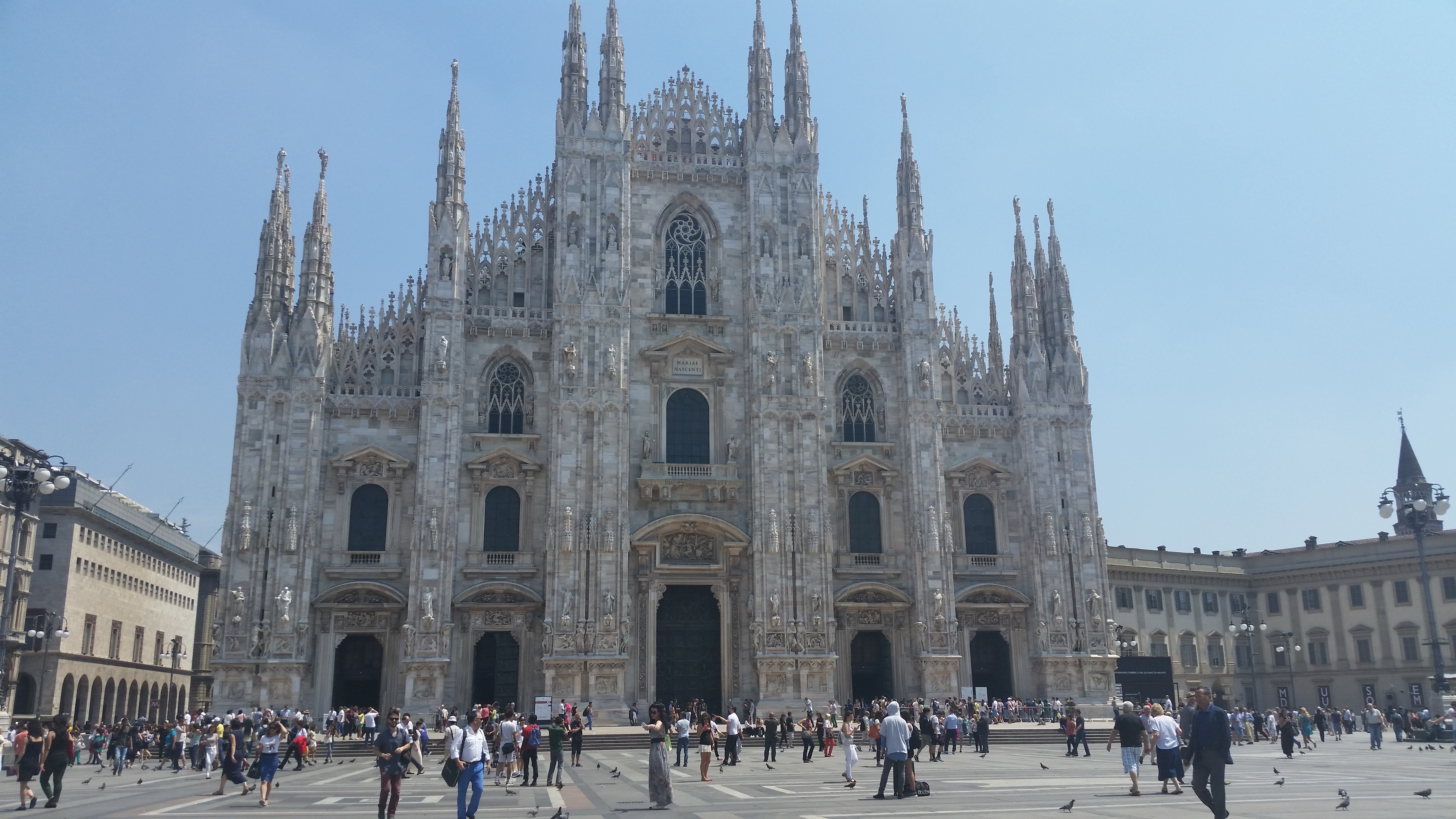 The Duomo di Milano, a large white marble Gothic cathedral with many spires, seen from Piazza del Duomo