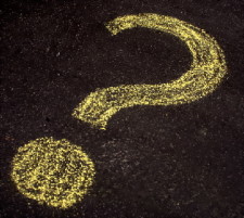 A question mark drawn in yellow chalk on black pavement