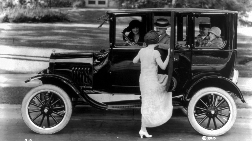 Picture of a Ford sedan with four passengers and a woman getting in on the driver's side in 1923.