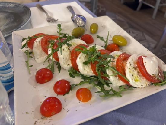 A plate featuring sliced mozzarella and tomatoes, garnished with arugula and cherry tomatoes.