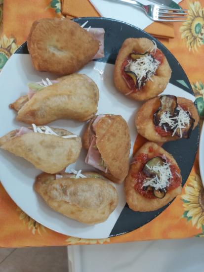 A plate with assorted fried snacks, including filled pastries and topped circular fritters, arranged on a colorful tablecloth.