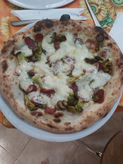 A round pizza topped with melted cheese, green peppers, and sliced pepperoni, served on a round plate.