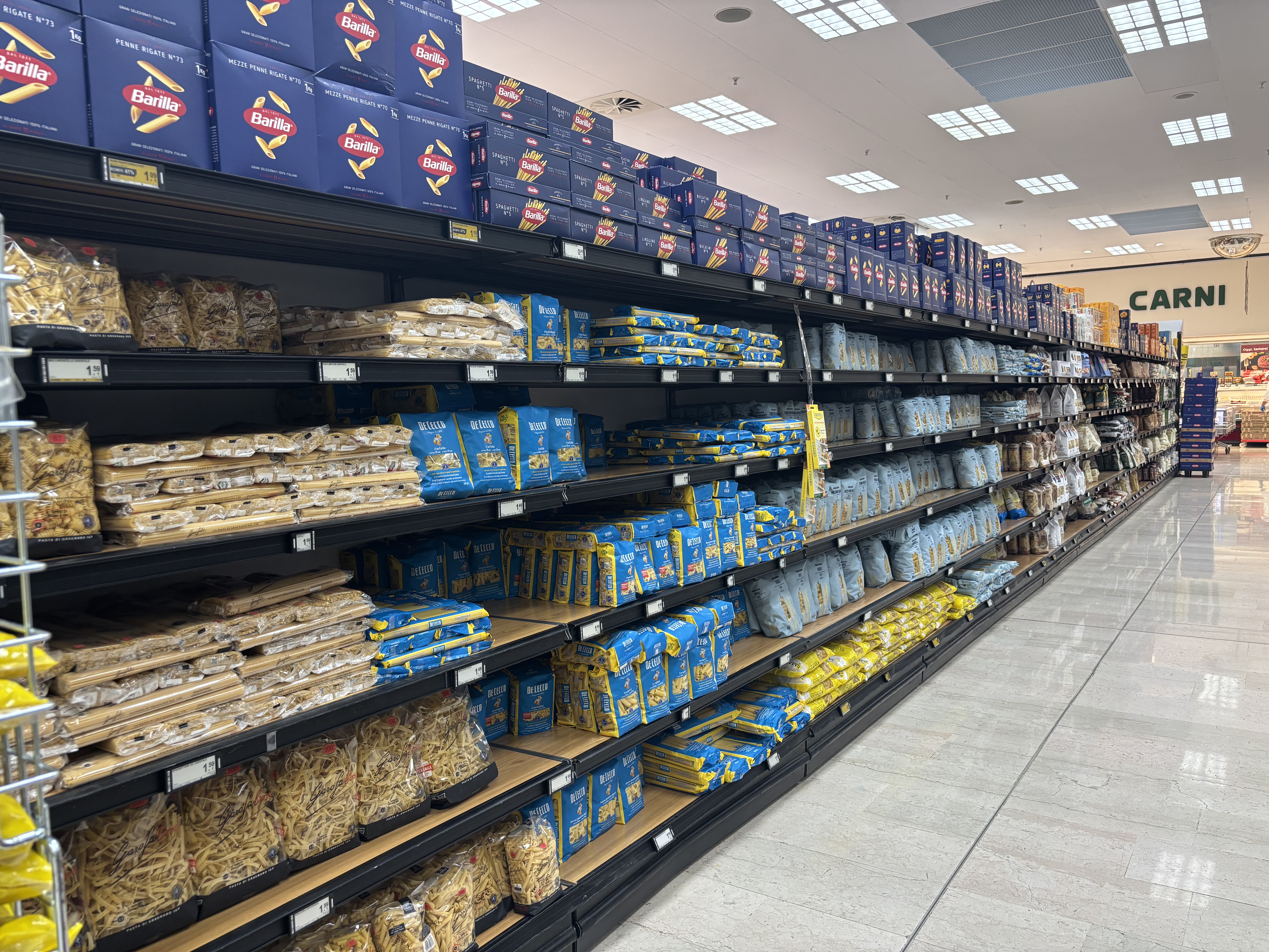 A supermarket aisle filled with various brands and types of pasta on shelves, including Barilla products.